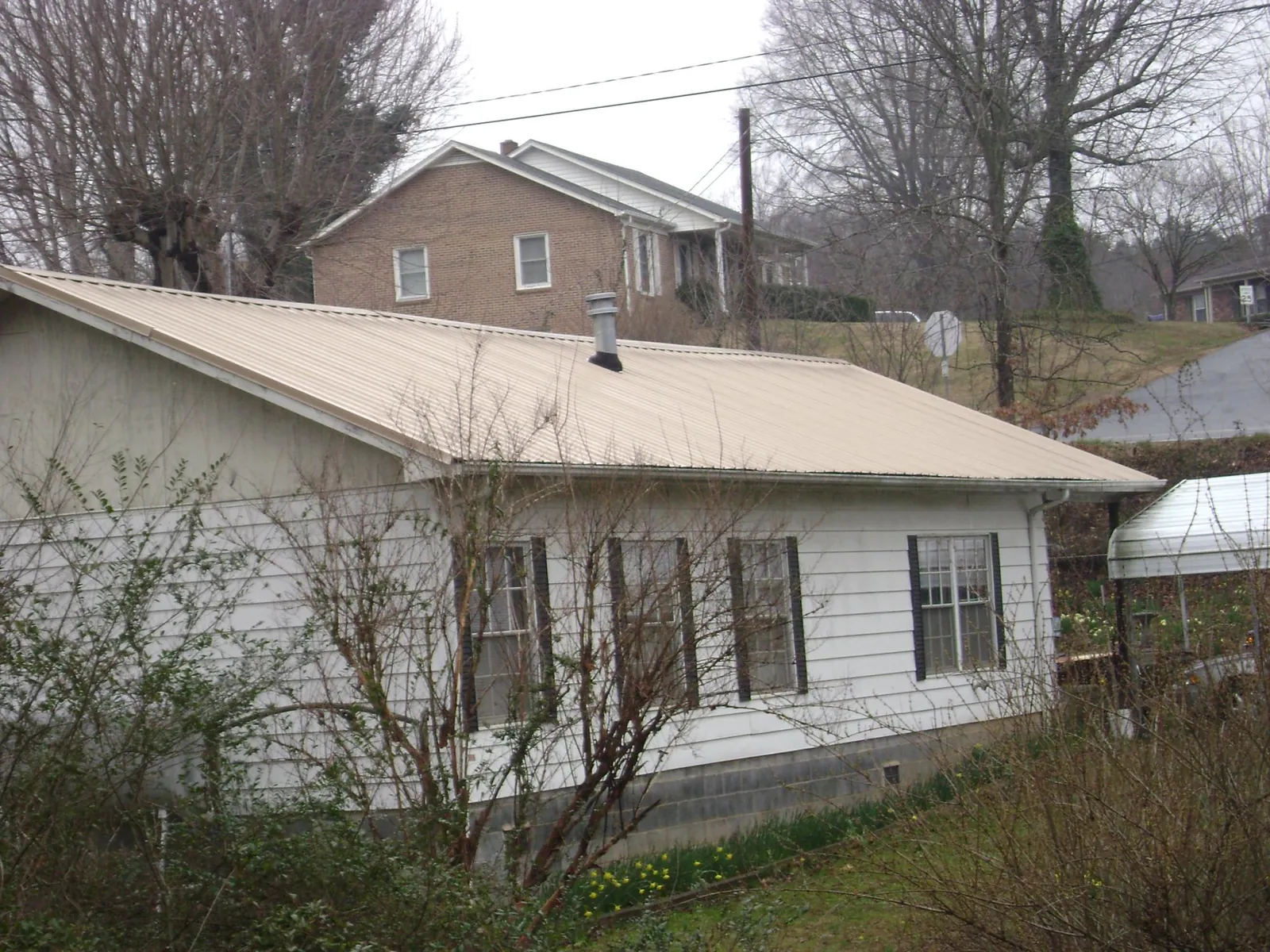 Tan metal roof on a white sided house set into a hillside — Commercial Roofing by Roofing Brothers in Elkton